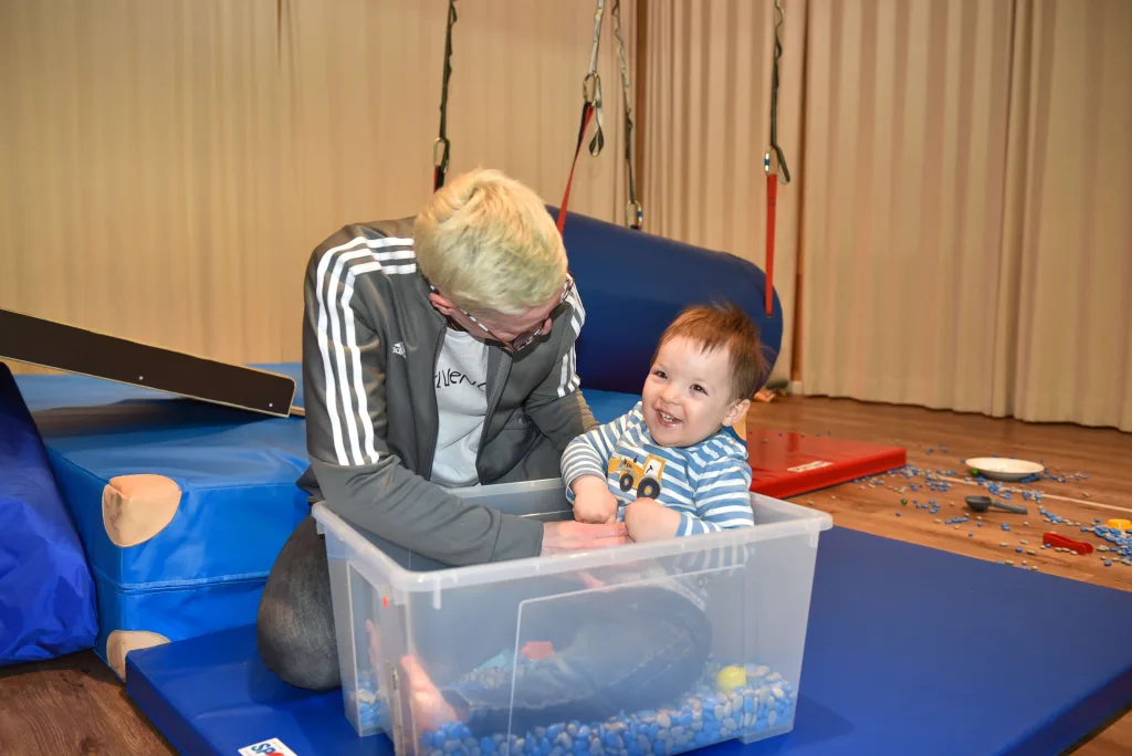 Fotoaufnahme eines Kindes zusammen mit einer Betreuerin im Innenbereich auf einer Wippe